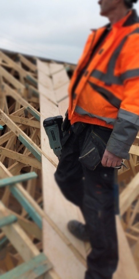 A carpenter stands in a roof valley wearing a High Visibility jacket and holding a Hitachi Koki Nail gun NR90GC2